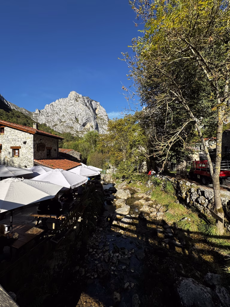 Bulnes de Abajo con el río Tejo cruzando el pueblo entre casas de piedra y montañas verdes.