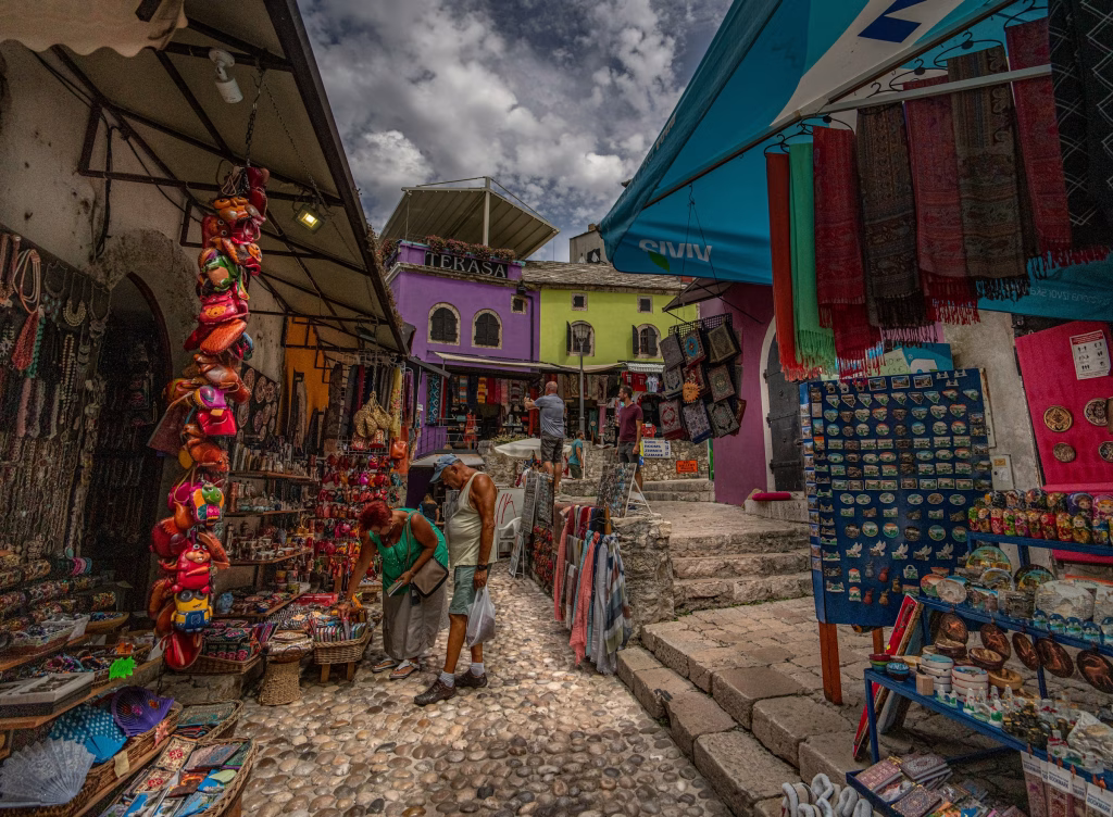 Calle empedrada con tiendas tradicionales y recuerdos en el casco antiguo de Mostar, llena de ambiente local y colorido.
